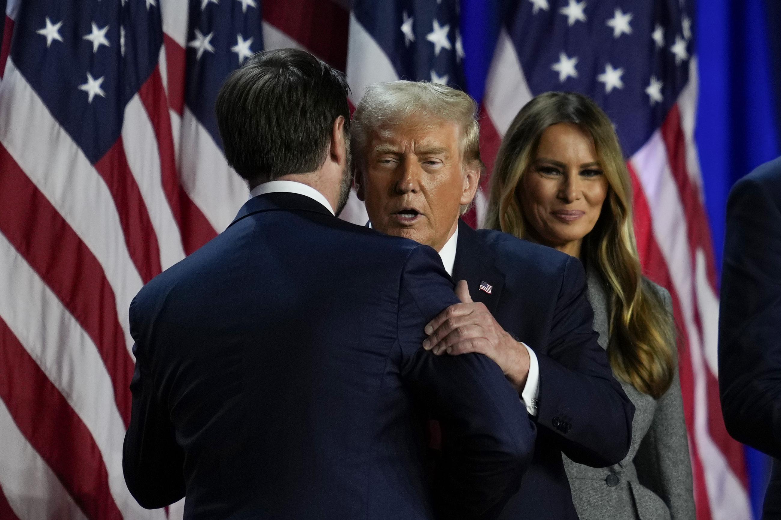 Republican presidential nominee former President Donald Trump, center, and Republican vice presidential nominee Sen. JD Vance, R-Ohio, embrace on stage at an election night watch party, Wednesday, Nov. 6, 2024, in West Palm Beach, Fla. (AP Photo/Julia Demaree Nikhinson)