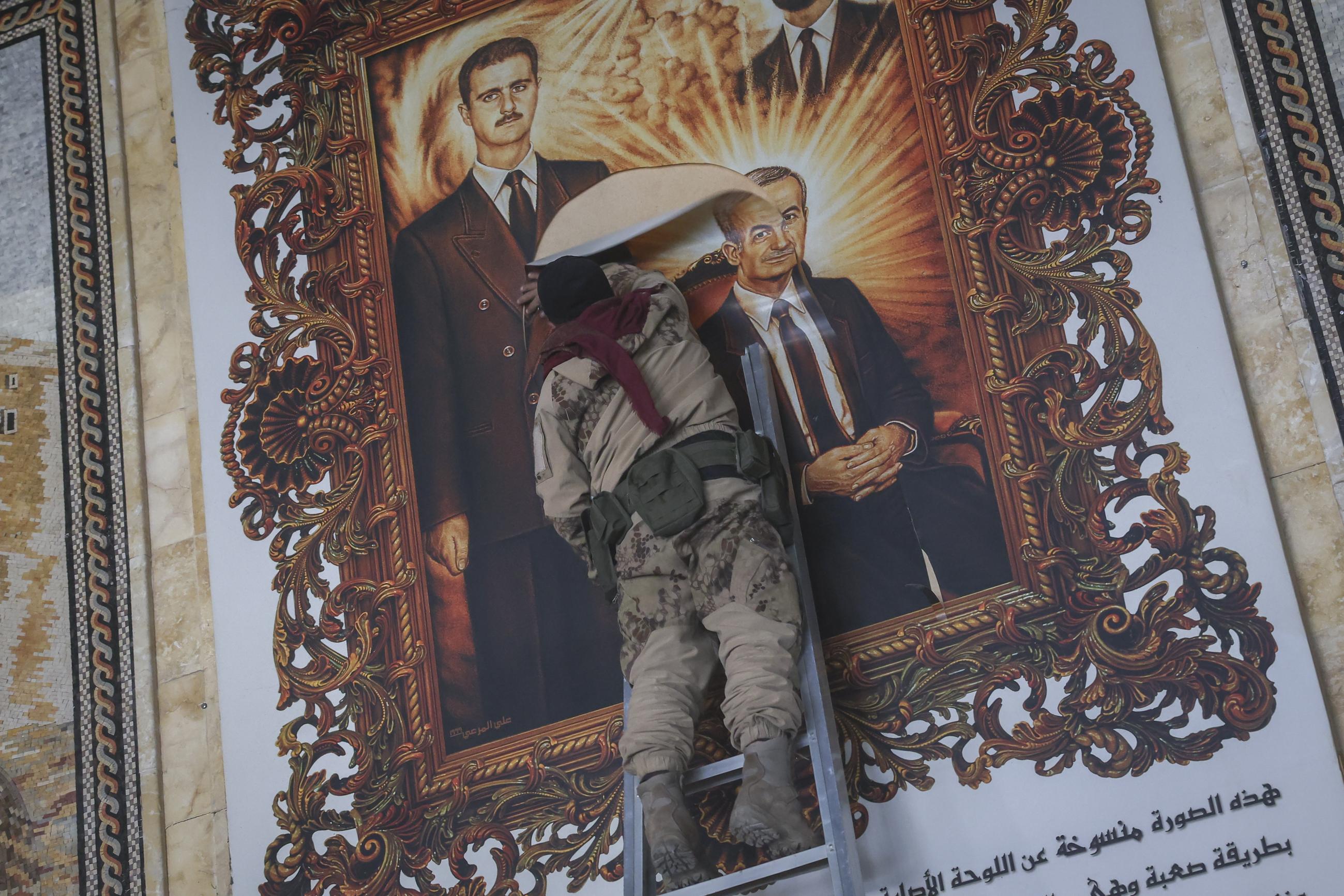 A Syrian opposition fighter tears at a painting depicting the country's overthrown president, Bashar al-Assad, and his late father, Hazef al-Assad, at Aleppo International Airport last week. (AP Photo/Ghaith Alsayed)
