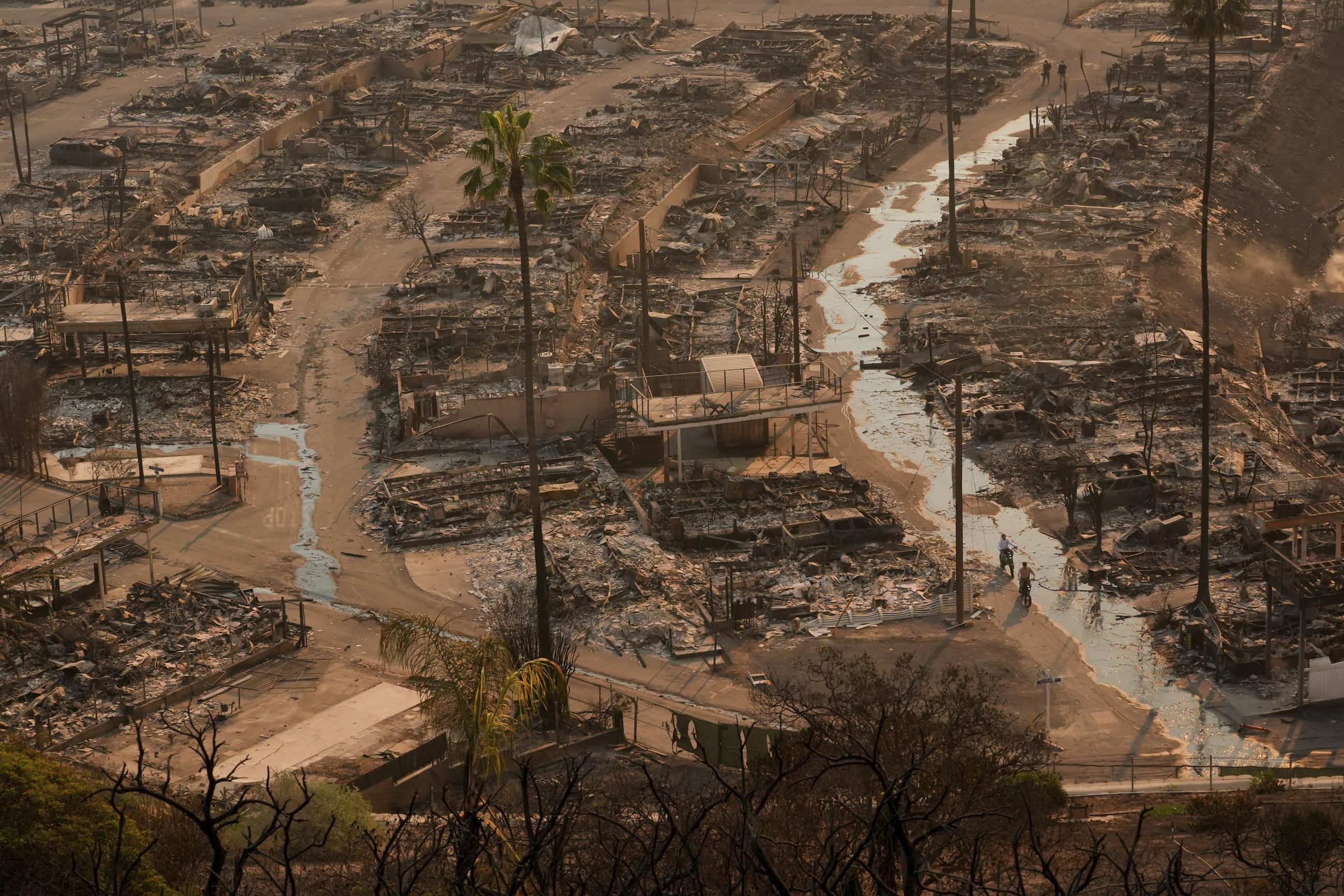 Two people ride bicycles amid the destruction left behind by a fire in the Pacific Palisades neighborhood of Los Angeles on Thursday. (AP Photo/Jae C. Hong)