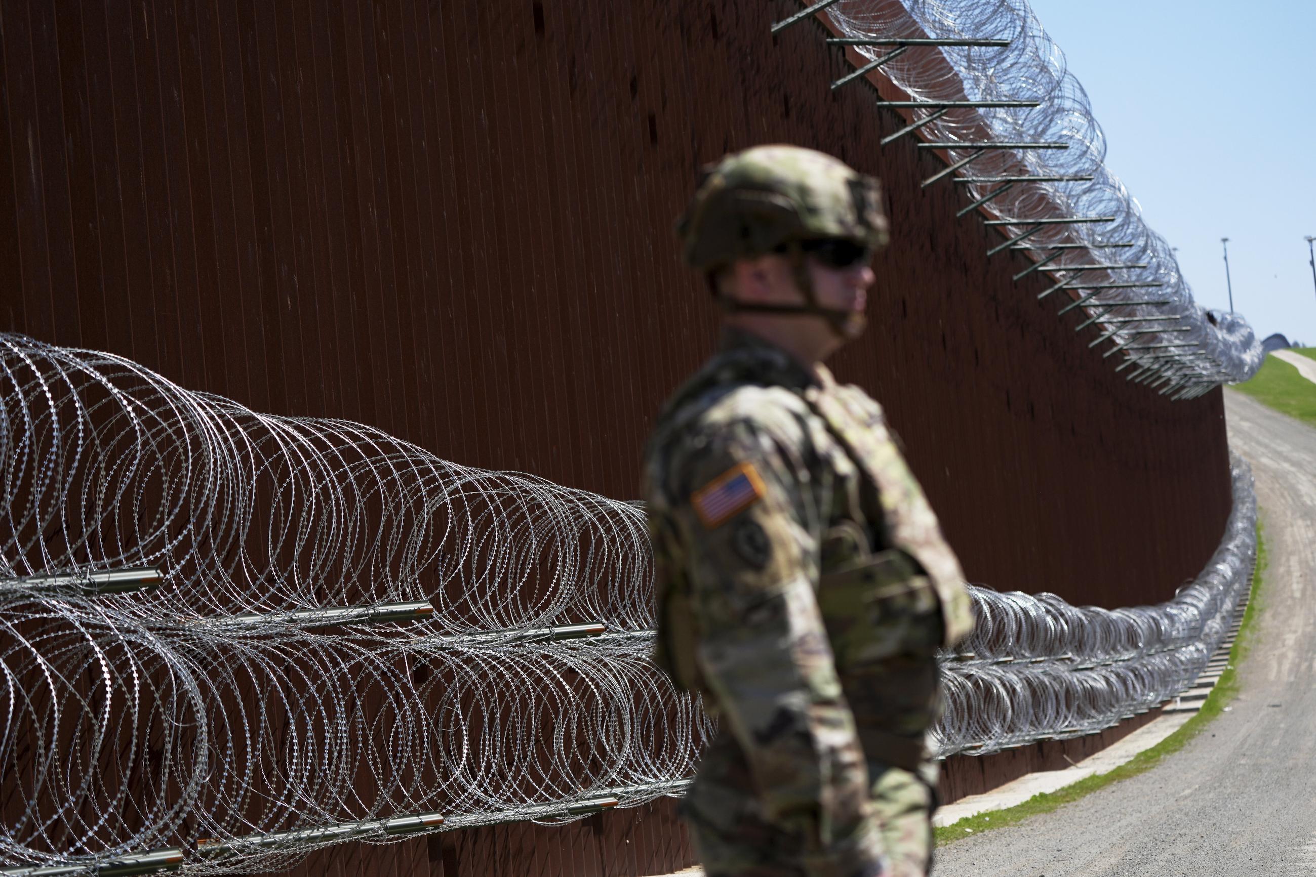A member of the military looks on in front of newly-installed concertina wire lining one of two border walls separating Mexico from the United States in March 2025. (AP Photo/Gregory Bull)