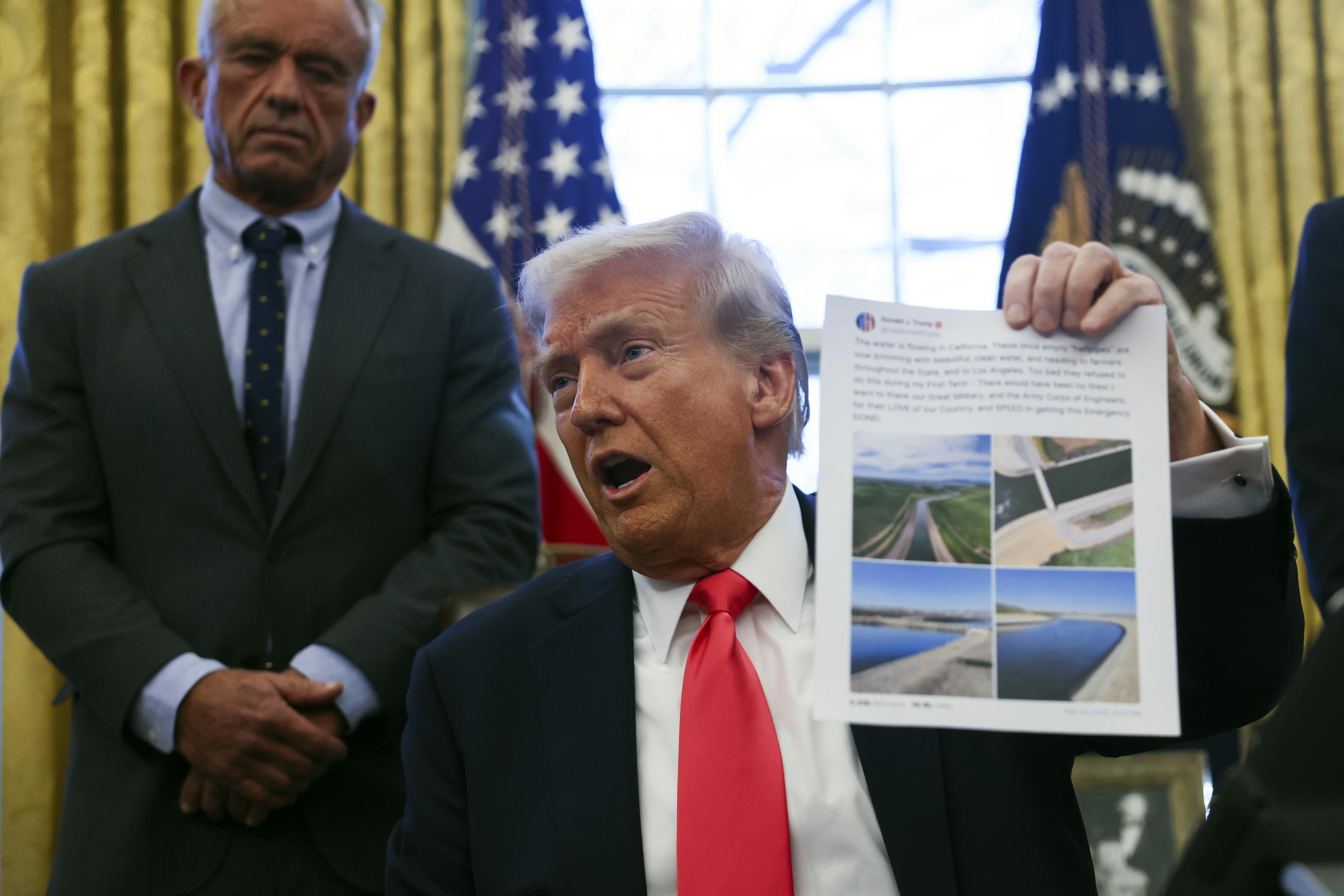 President Donald Trump holds up a Truth Social post on California water as he talks with reporters in the Oval Office at the White House in Washington, Tuesday, Feb. 25, 2025. (Pool via AP)