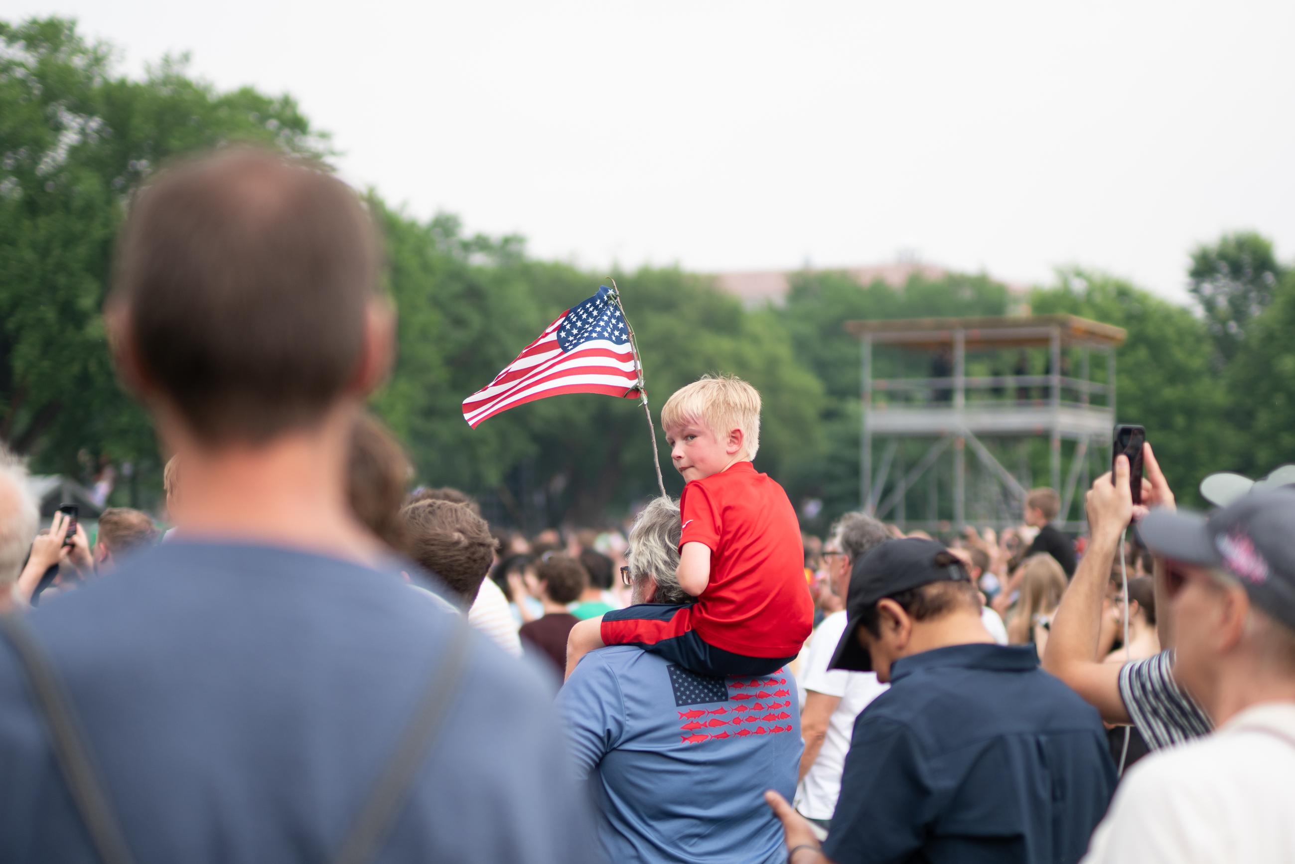The Army's 250th Birthday parade attendee holds up a makeshift American Flag taped to a twig shortly before the parade festivities began. June 15, 2025.