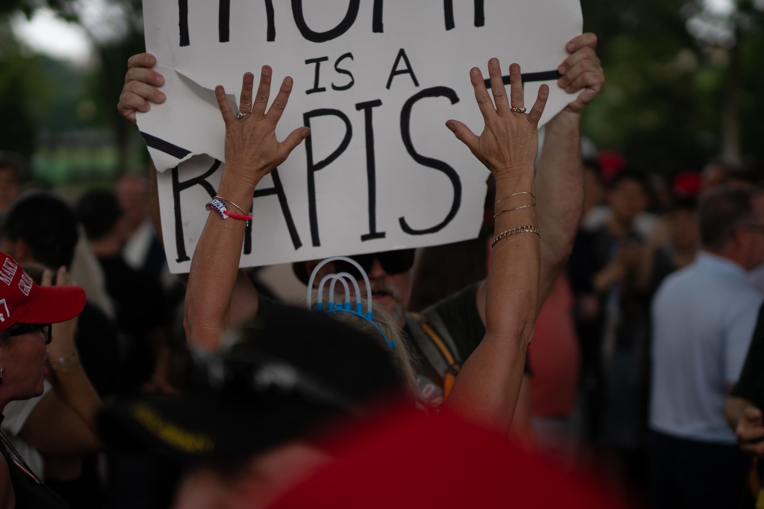 A counter protesters holding up a “TRUMP IS A RAPIST” sign is obstructed by another attendee. June 15, 2025.