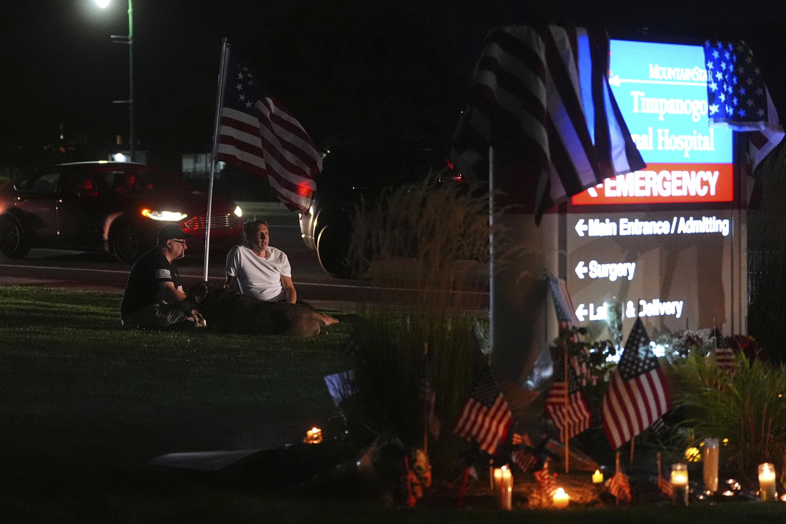 Brian Colton, left, sits with dog Louie and Skyler Baird, right, who was a close witness of the shooting, as they visit a growing memorial for Charlie Kirk outside Timpanogos Regional Hospital after Kirk was shot and killed Wednesday, Sept. 10, 2025, in Orem, Utah. (AP Photo/Lindsey Wasson)