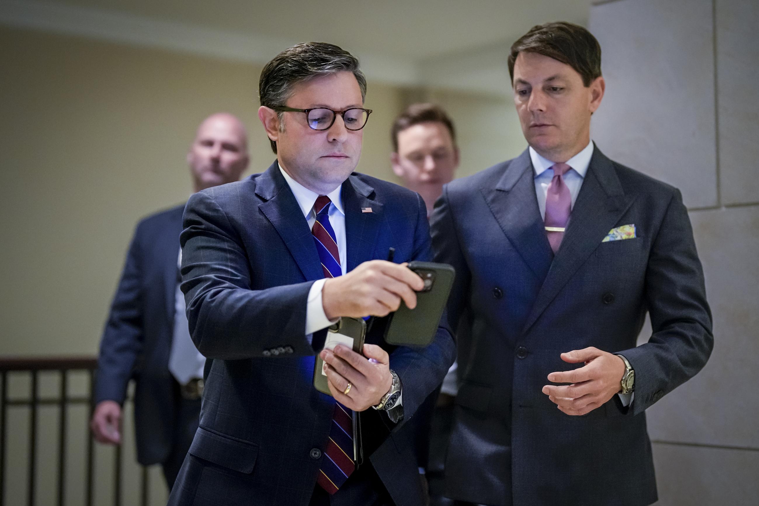House Speaker Mike Johnson checks a phone handed to him by political aide Hogan Gidley as he arrives to talk with reporters at the Capitol on April 1. (AP Photo/J. Scott Applewhite)