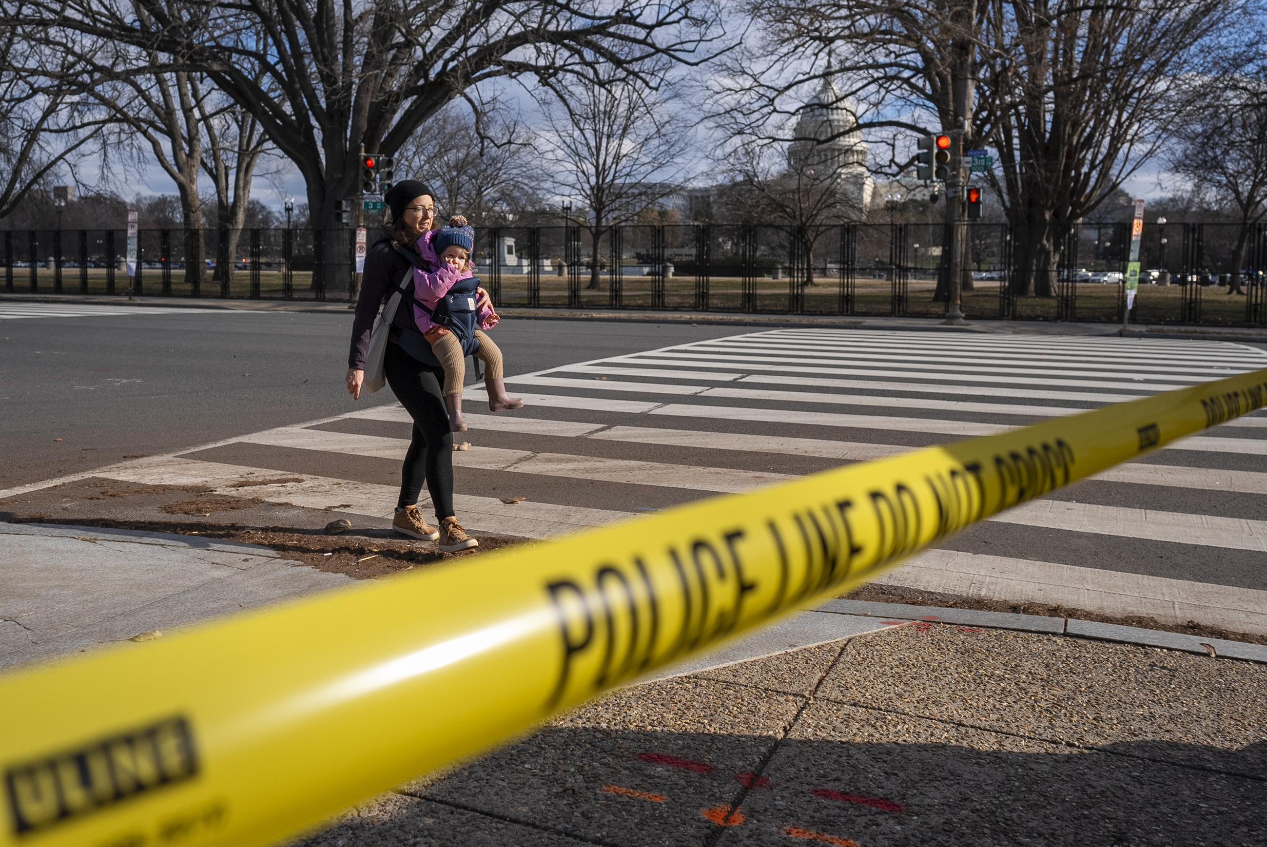 A woman with a baby crosses the street by police tape, near the U.S. Capitol on Jan. 2 as police investigate a suspicious vehicle near the Capitol building. (AP Photo/Jacquelyn Martin)
