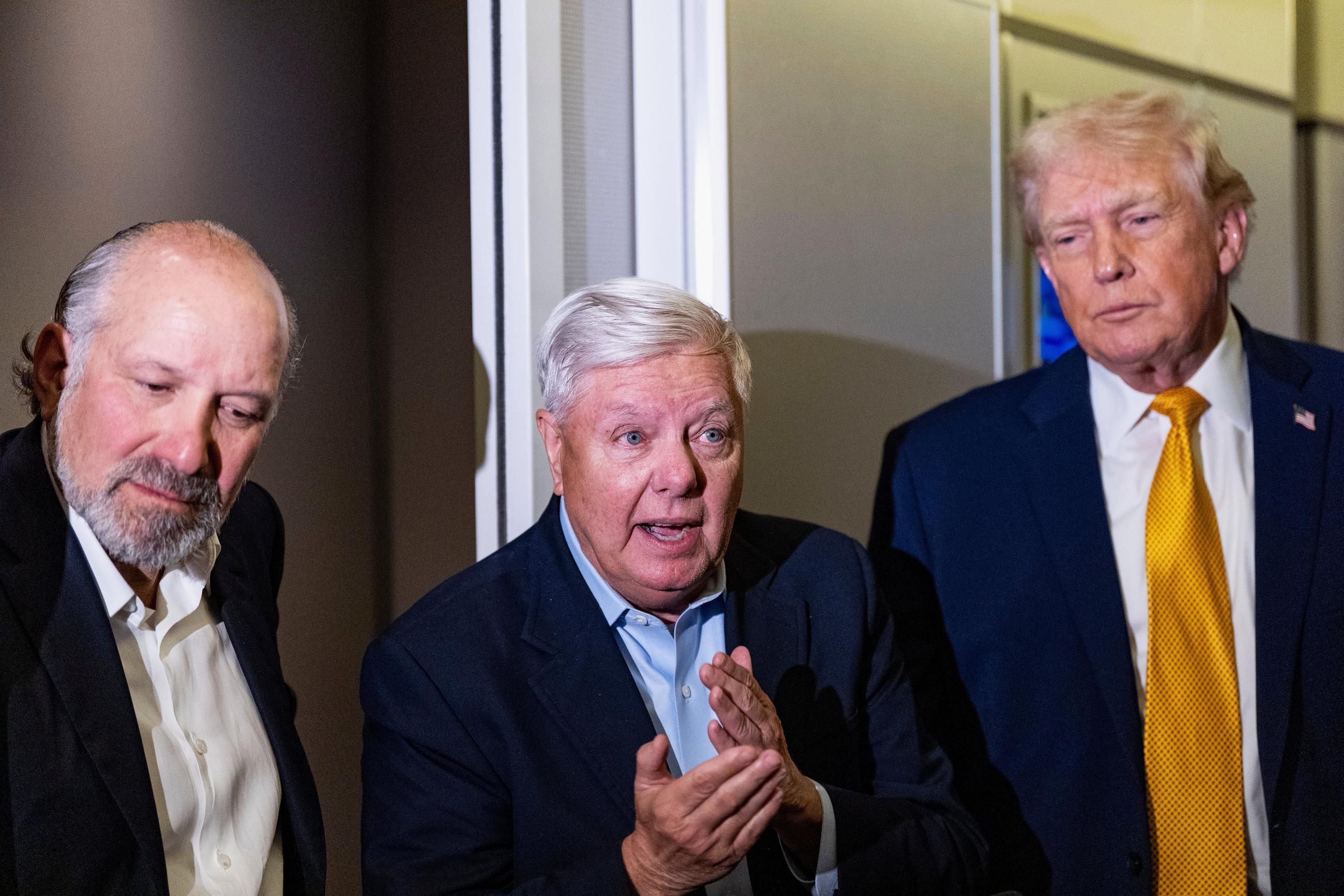 President Trump, accompanied by Commerce Secretary Howard Lutnick and Sen. Lindsey Graham, speaks with reporters while in flight on Air Force One on Jan. 4. (AP Photo/Alex Brandon)