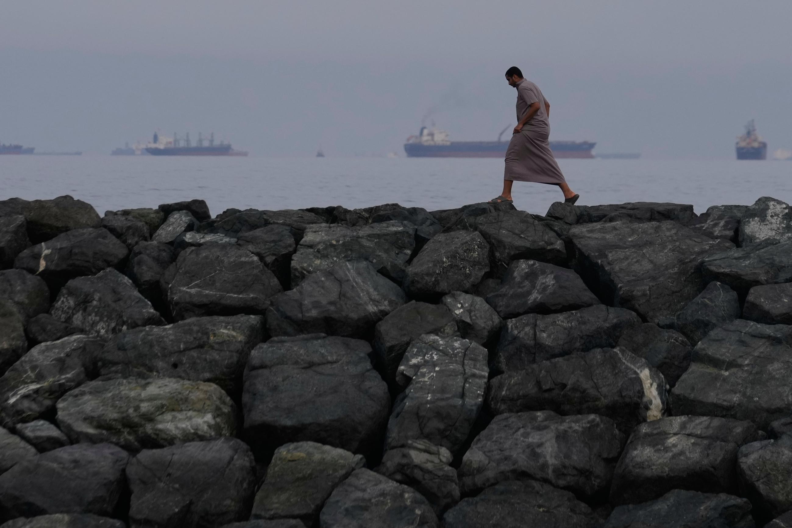 A man walks along the shore as oil tankers and cargo ships line up in the Strait of Hormuz, as seen from Khor Fakkan, United Arab Emirates, on March 11. (AP Photo/Altaf Qadri)
