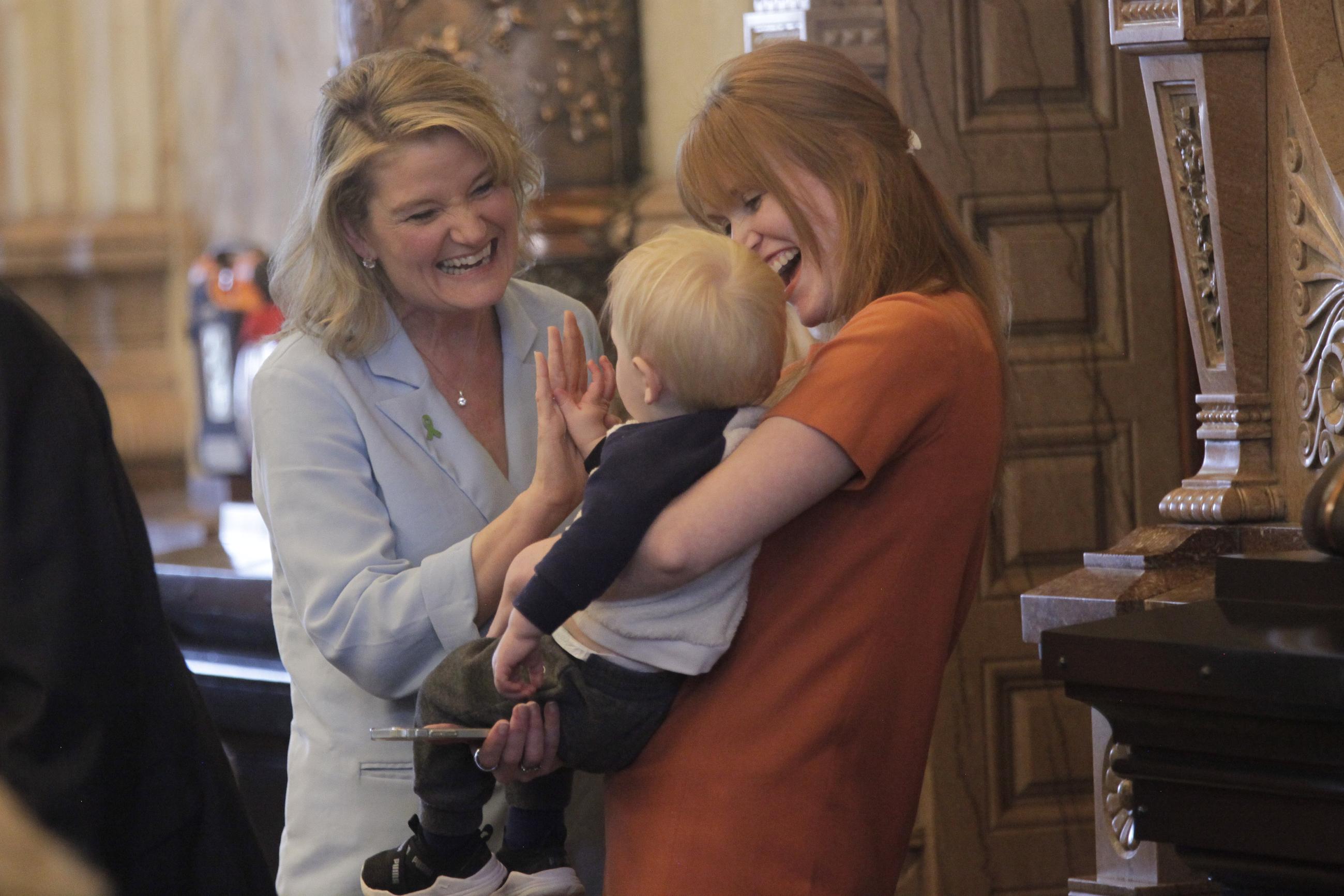 Kansas state Sen. Cindy Holscher, left, D-Overland Park, gives a high-five to Leland, the young son of Sen. Kristen O'Shea, right, R-Topeka, during a session of the Senate, Wednesday, March 29, 2023, at the Statehouse in Topeka, Kan. Lawmakers are preparing for an intense four days of work ahead of their annual "Drop Dead Day" deadline. (AP Photo/John Hanna)