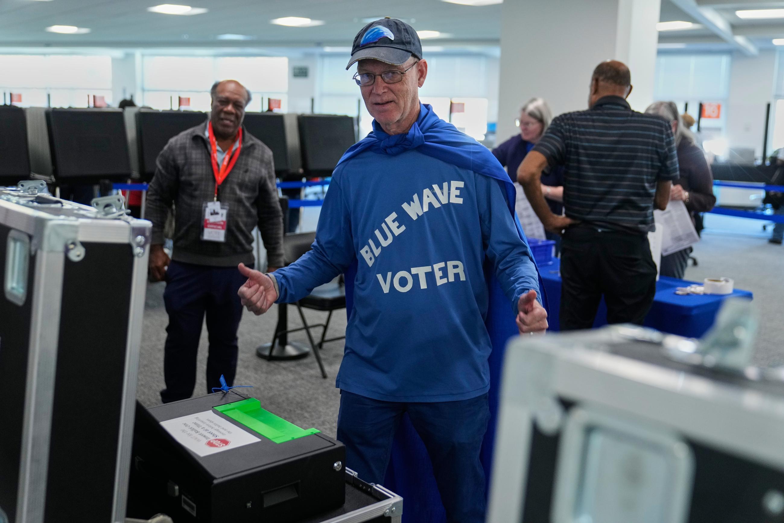 Steven Fitz, wearing a blue cape and a shirt that reads "blue wave voter" gestures after scanning his ballot at early in-person voting in Cleveland, Wednesday, Oct. 7, 2026. (AP Photo/Sue Ogrocki)